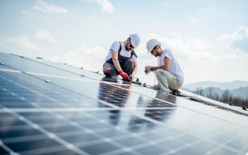 Team of two workers on a house's roof installing solar panels.
