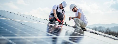 Team of two workers on a house's roof installing solar panels.